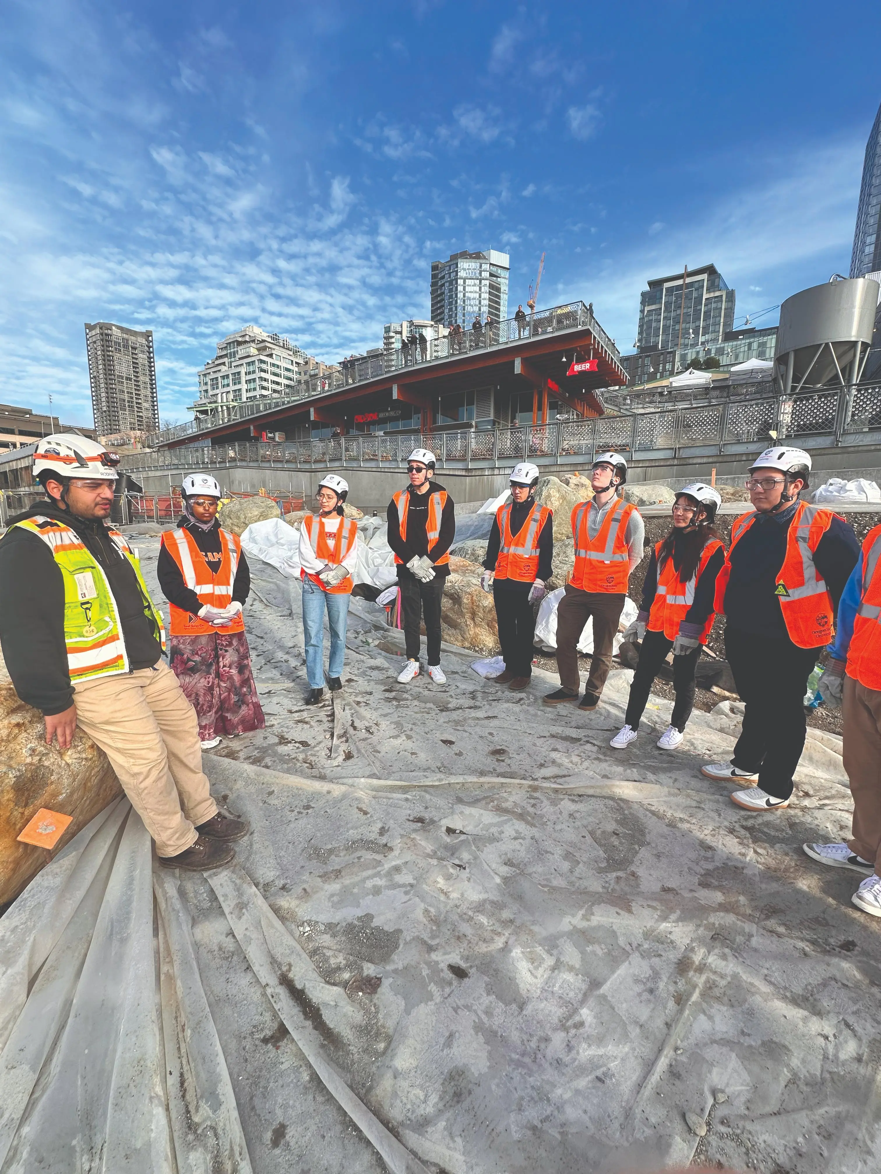 Group of adults in orange safety vests stand on a construction site.