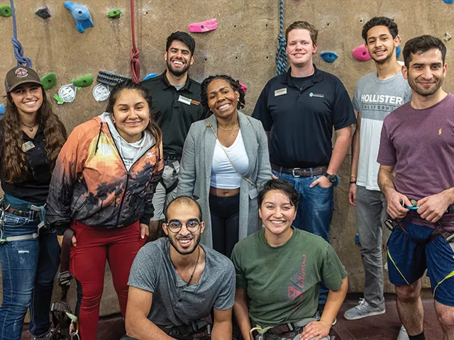 Group of students standing in front of an indoor climbing rock wall