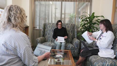 Three people meet to discuss notes on upholstered furniture in a consultation room.