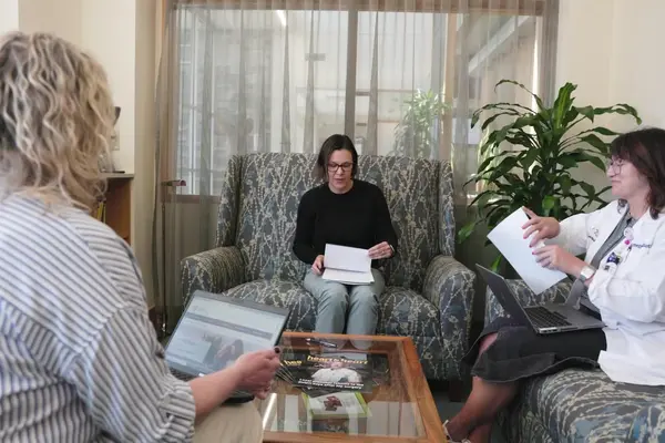 Three people meet to discuss notes on upholstered furniture in a consultation room.